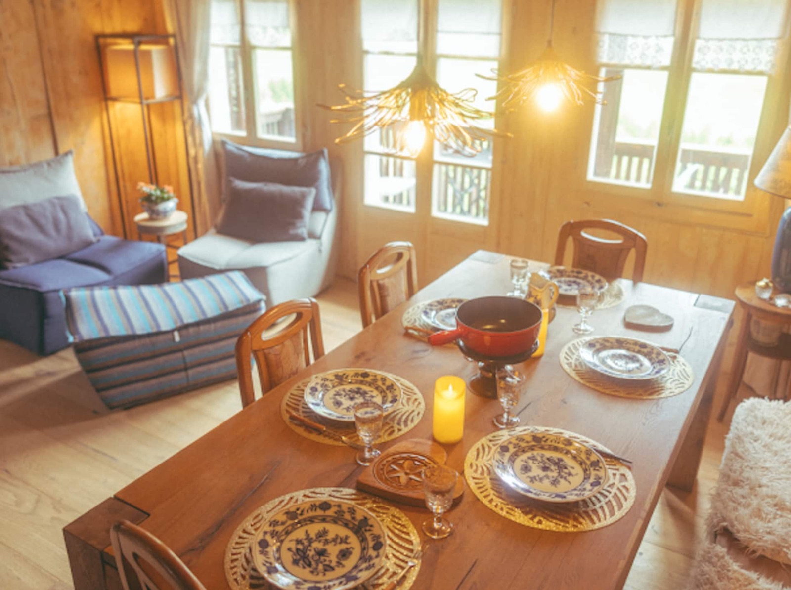 The long table set by candlelight, glass pendant lamps glowing above and the valley windows beyond.